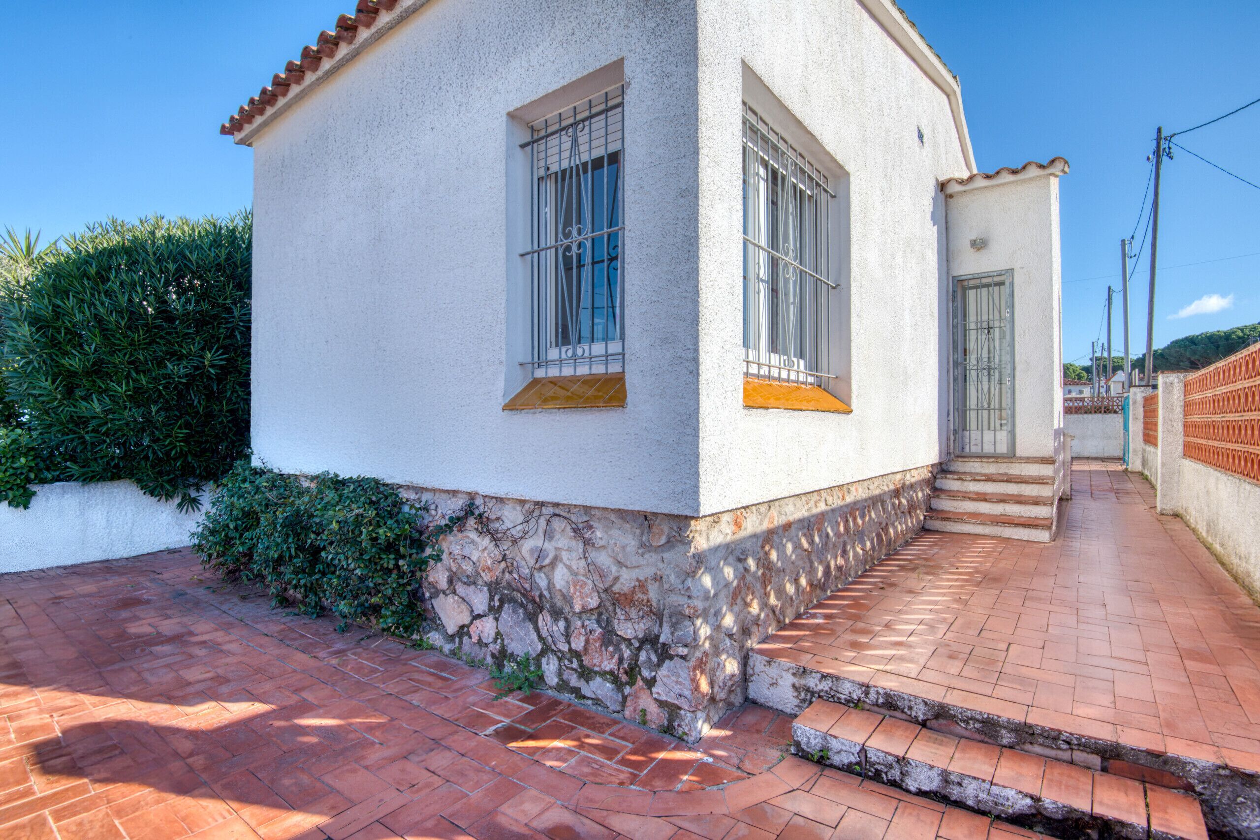 Un bâtiment blanc avec un socle en pierre, une terrasse carrelée et un portail en métal.