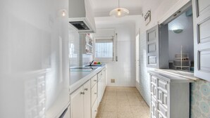 A narrow kitchen with white cabinets, a tiled backsplash, and a window with blinds. - MIRAVETTE: Cozy house in L’Escala near the harbor (L'Escala)