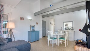 A living room with a sofa, a dining table with chairs, a small kitchen area with a microwave, and a television. - MIRAVETTE: Cozy house in L’Escala near the harbor (L'Escala)
