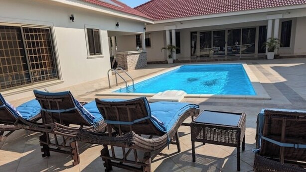 Una piscina con sillas de descanso y una mesa, rodeada por un porche cubierto.