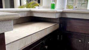 Un rincón de una habitación con un banco de piedra, un armario de madera oscura y una ventana con plantas afuera.