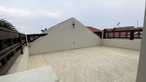 Una terraza en la azotea con suelo de baldosas, barandilla y estructura de techo triangular.