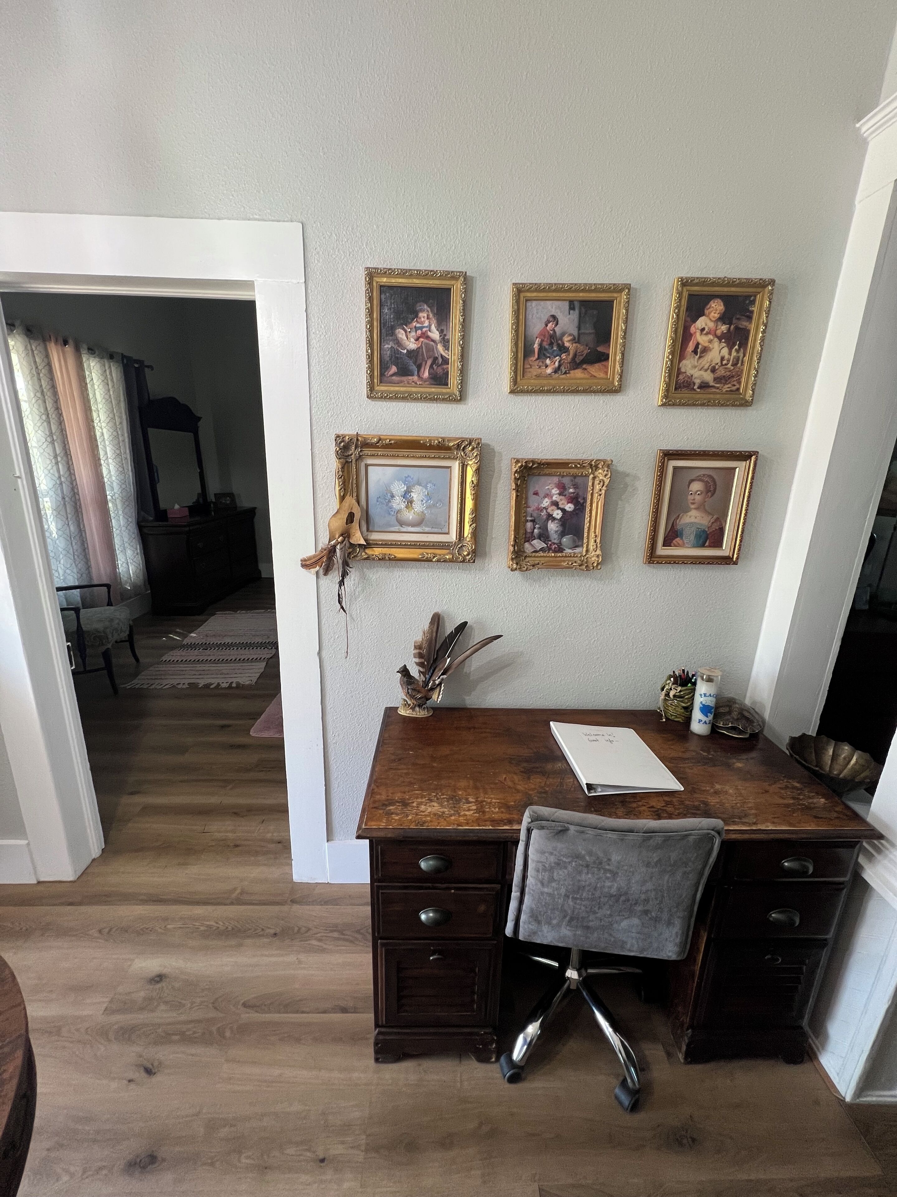Una habitación con un escritorio de madera, una silla y una pared decorada con fotografías enmarcadas.