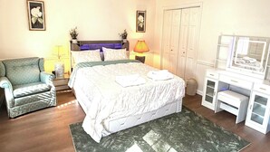 A bedroom with a bed, a chair, a desk with a mirror, and a ceiling fan.