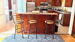 A kitchen with a central island, bar stools, a refrigerator, a microwave, and a stove.