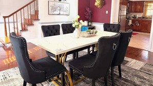 A dining area with a white table, black upholstered chairs with gold studs, a chandelier, and a red accent wall.