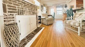 Ein geräumiges Wohnzimmer mit Kamin aus Ziegelsteinen, Deckenventilator und Holzboden.