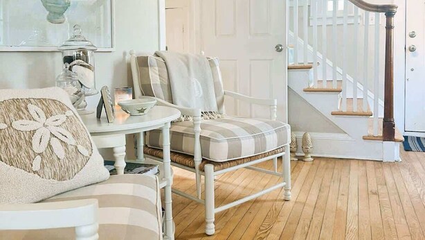 Ein geräumiges Zimmer mit Holzboden, einer weißen Treppe und einer Sitzecke mit Sessel und Tisch.
