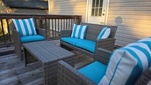 Un área de estar exterior de mimbre con cojines azules y una terraza de madera.