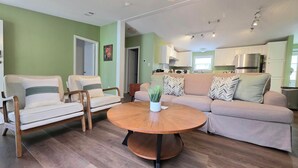 Un salón con una mesa redonda de madera, dos sofás con cojines estampados y una pared verde.