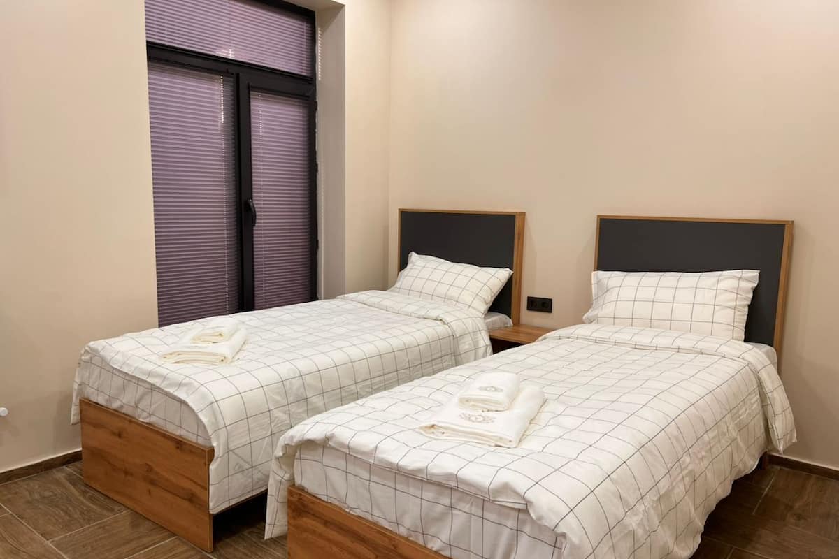 Een slaapkamer met twee eenpersoonsbedden, elk met een houten hoofdbord en een wit sprei met een subtiel dessin.