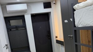 A room with a bunk bed, a black door, a window with blinds, and an air conditioning unit. - Boutique Hotel 108 (Bishkek)