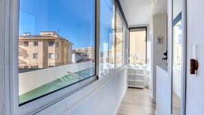 Un pasillo estrecho con amplios ventanales, vistas a edificios y una piscina en el exterior.