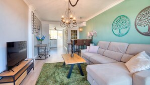 Una sala de estar moderna con un televisor de pantalla plana, un sofá color beige, una mesa de centro de madera y una alfombra verde.