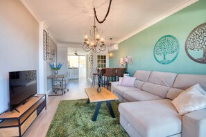 Ein modernes Wohnzimmer mit einem Flachbildfernseher, einem beige farbenen Sofa, einem Holztisch und einem grünen Teppich.