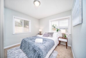 A bedroom with a bed, two bedside tables, a nightstand, a window with blinds, and a ceiling light. - Game On! Endless Games & Huge Backyard w Parking! (San Diego)