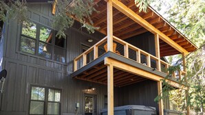 Eine zweistöckige Holzhütte mit Balkon, großen Fenstern und einer überdachten Terrasse.