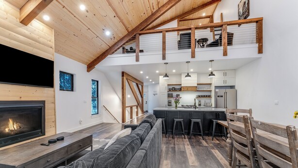 Ein moderner Loft-Wohnraum mit großem Kamin, einer gemütlichen Sitzecke, einer Küche mit Barhocker und einer erhöhten Galerie mit Treppe.