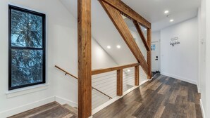 Ein modernes Interieur mit einer Holztreppe, einem großen Fenster mit Blick auf Bäume und einer weißen Wand mit Kleiderhaken.