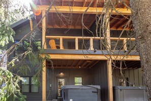 A two-story wooden cabin with a balcony, large windows, and a covered outdoor area. - New Build Ski in/Ski Out House w/Hot Tub (Whitefish)