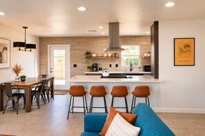 A modern kitchen with a central island, bar stools, and a dining area with a table and chairs. - Downtown, Stargazing Deck, Fire Pit, Record Player, Games (Joshua Tree)
