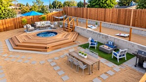 Un patio trasero con jacuzzi, mobiliario exterior, una parrilla y una terraza de madera.