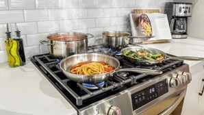 Uma cozinha com fogão a gás, panelas, frigideiras e um livro de receitas.