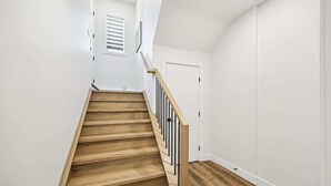 A staircase with wooden steps and black railings leading to a white door. - Steps to Transit • Bright Kitchen • Parks & Shops (Calgary)