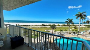 A balcony with a view of a beach, a pool, and palm trees. - Estero Beach & Tennis 205B - Beach View (Fort Myers Beach)
