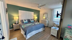 Ein Schlafzimmer mit einem Bett, Nachttischen, einer Kommode, einem Spiegel und einem Deckenventilator.