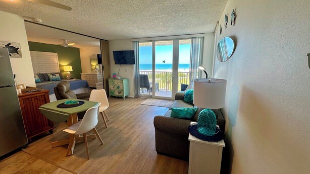 A compact living space with a dining area, a sofa, a small table, and a balcony with a view of the sea. - Estero Beach & Tennis 205B - Beach View (Fort Myers Beach)