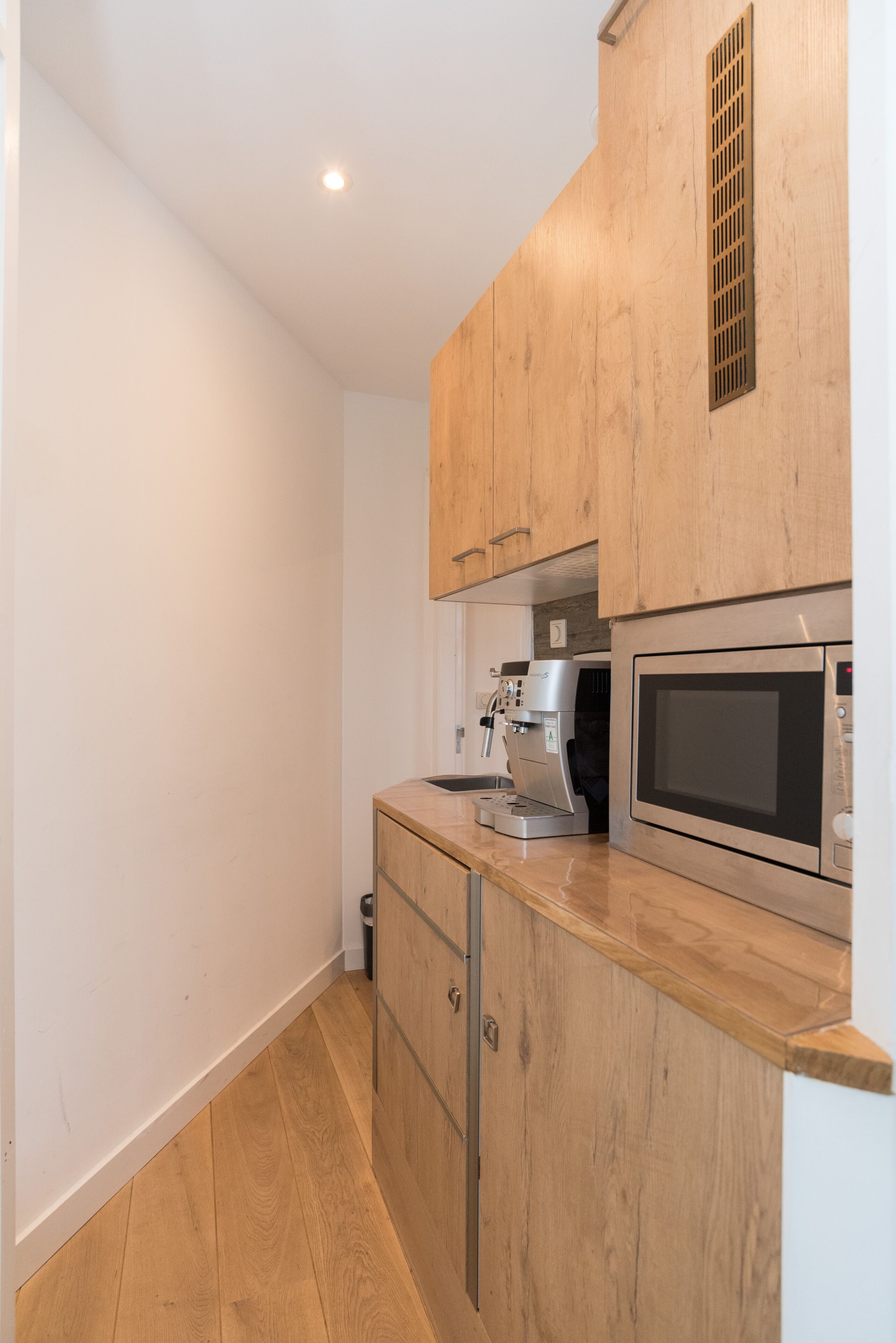 A compact kitchen with wooden cabinets, a built-in microwave, and a coffee machine.