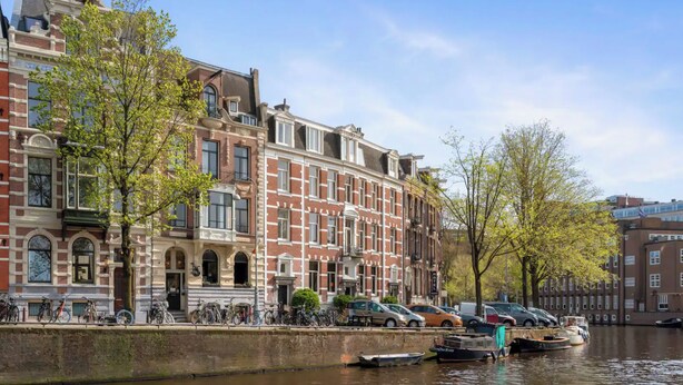A canal-side building with a row of parked bicycles and a row of parked cars along the water. - Canal view home in the heart of Amsterdam (Amsterdam)