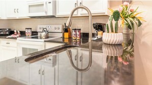 Cozinha com torneira de aço inoxidável, armários brancos e bancada com um vaso de flores.