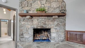 Ein Steinkamin mit hölzernem Sims, einer Topfpflanze und Feuer.