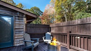 A wooden deck with a metal fire pit, two Adirondack chairs, and a wooden fence. - Farm Suite, King bed, firepit, BBQ grill, animals! (Asheville)