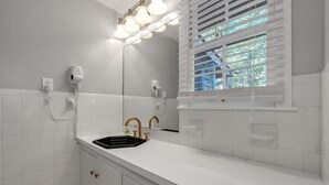 A bathroom with a white tiled wall, a black sink, gold faucets, a mirror, and a window with blinds. - Farm Suite, King bed, firepit, BBQ grill, animals! (Asheville)
