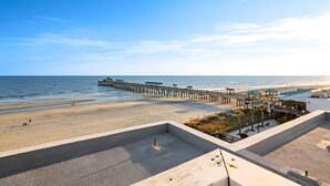 Ein Strand mit einer Holzstege, der sich ins Meer erstreckt, ein Sandstrandbereich und ein Strandabschnitt mit Sonnenschirmen und Liegestühlen.