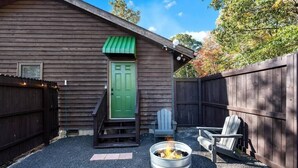 Een houten hut met een groene deur, een vuurkuil en twee Adirondack-stoelen.