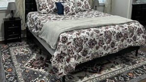 Ein Schlafzimmer mit einem Bett, einem Deckenventilator, einem Nachttisch, einem Teppich und einem Bild an der Wand.