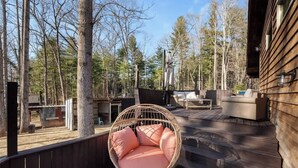 En træterrasse med en fletstol og hynder, omgivet af træer.