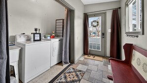 A laundry area with a washing machine, drying rack, and a small window with curtains.