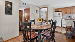 A dining area with a round wooden table, black chairs with plaid cushions, and a vase with sunflowers.