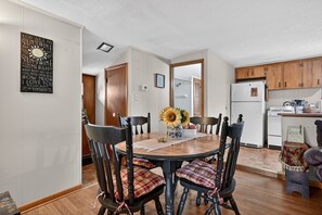 Un comedor con una mesa redonda de madera, sillas negras con cojines de cuadros y un florero con girasoles.
