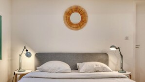 Ein ordentlich bezogenes Bett mit weißen Leinentüchern, zwei Nachttischlampen und einer runden Wanddekoration.