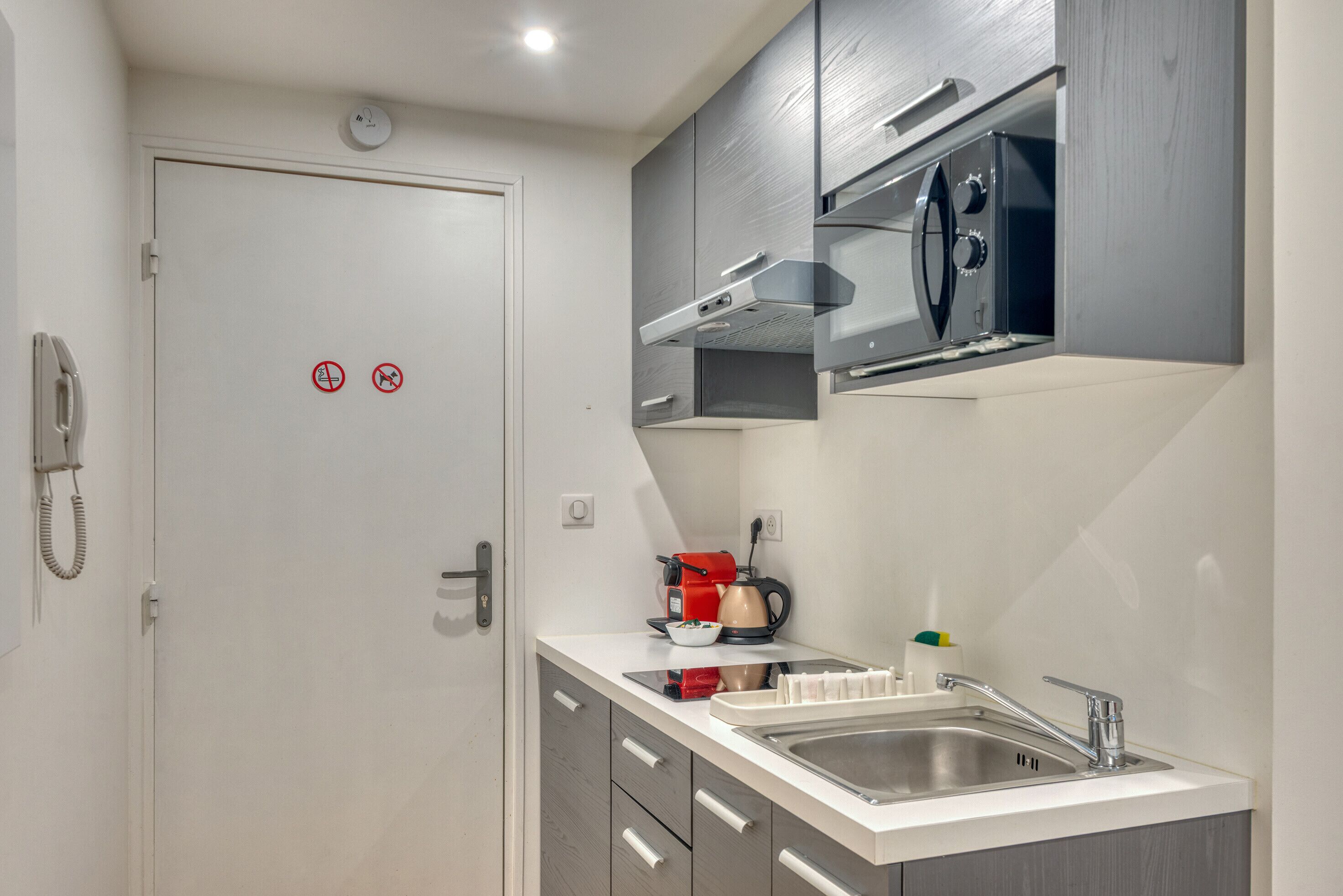 Una cocina compacta con horno empotrado, cafetera y lavamanos.
