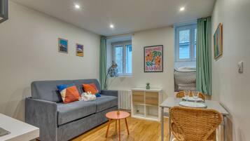 A compact living space with a grey sofa, a small round table, a wicker chair, and a white cabinet.