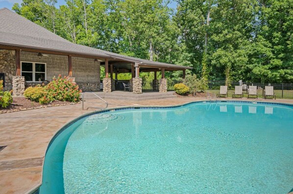 A swimming pool with a covered patio area, stone walls, and a view of trees. - Mcdonald Lakeside Cottage (Sevierville)