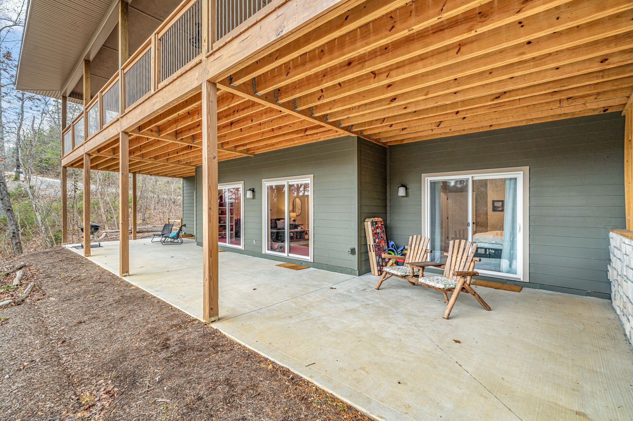 Une terrasse couverte avec des poutres en bois, un sol en béton et des sièges d’extérieur.