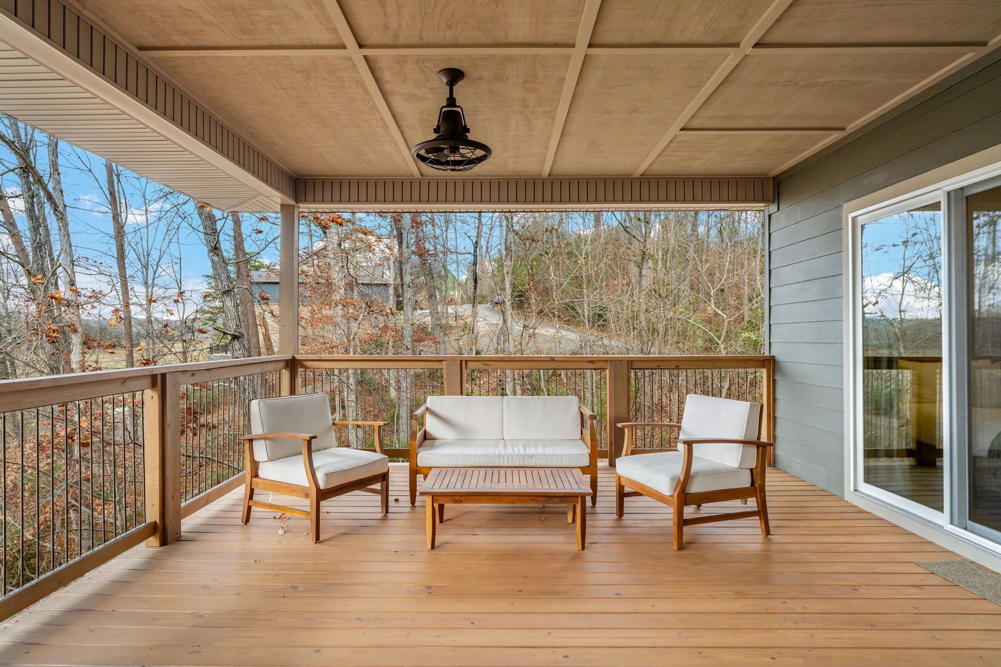 A covered deck with a wooden floor, a ceiling fan, and a sofa with two chairs.